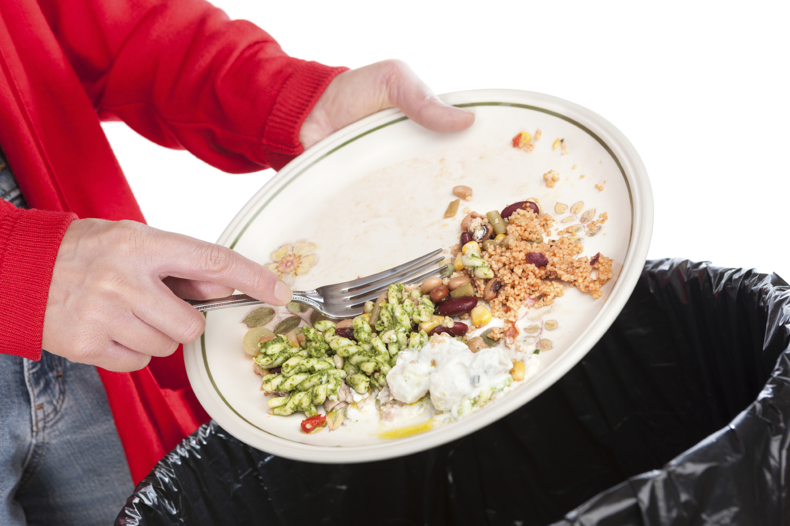 Close-up of a woman sweeping the leftovers from a meal into a garbage bin. The background is pure white.